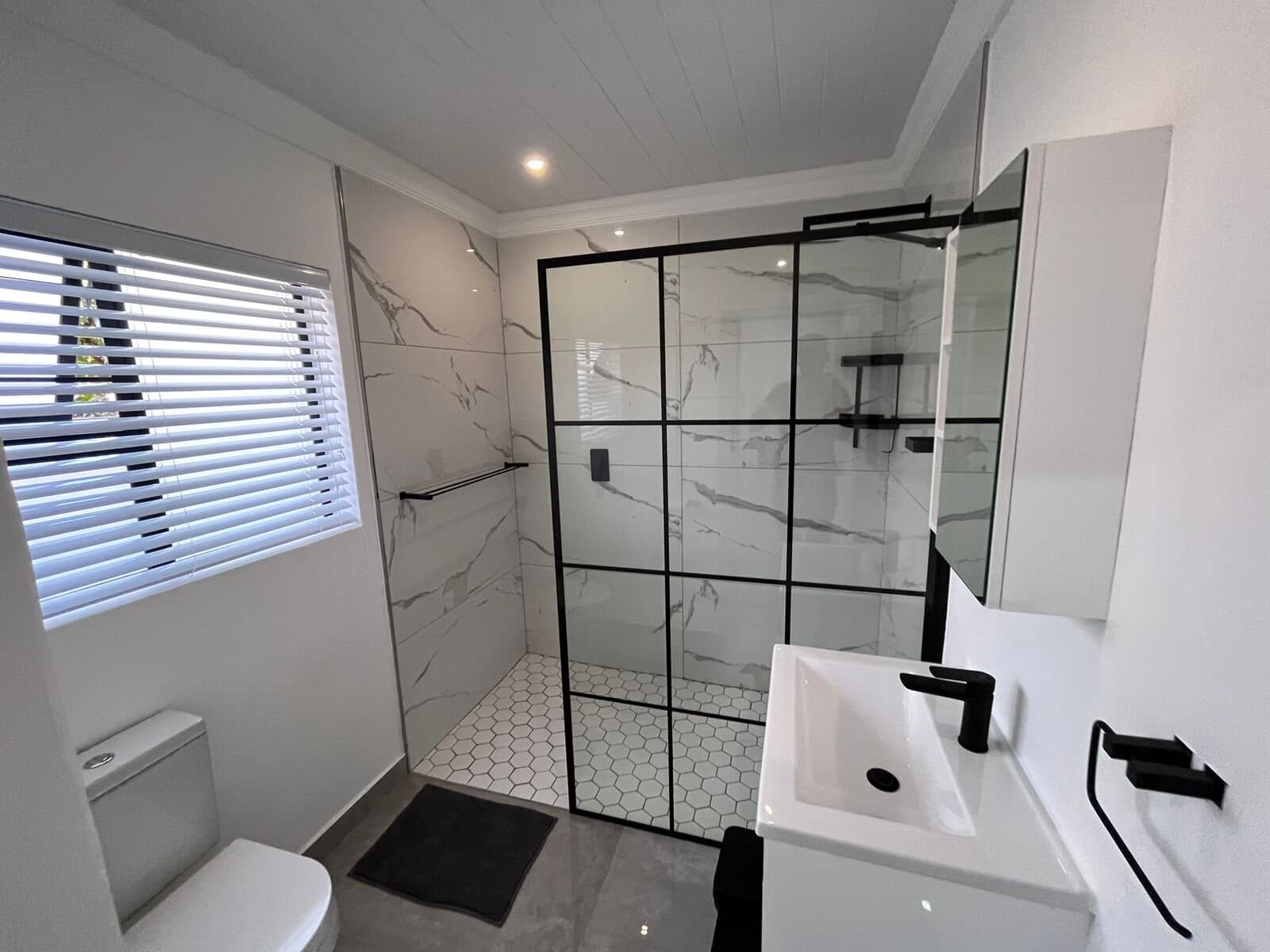Bathroom renovation with a black-framed glass shower, marble-look tile and floating vanity