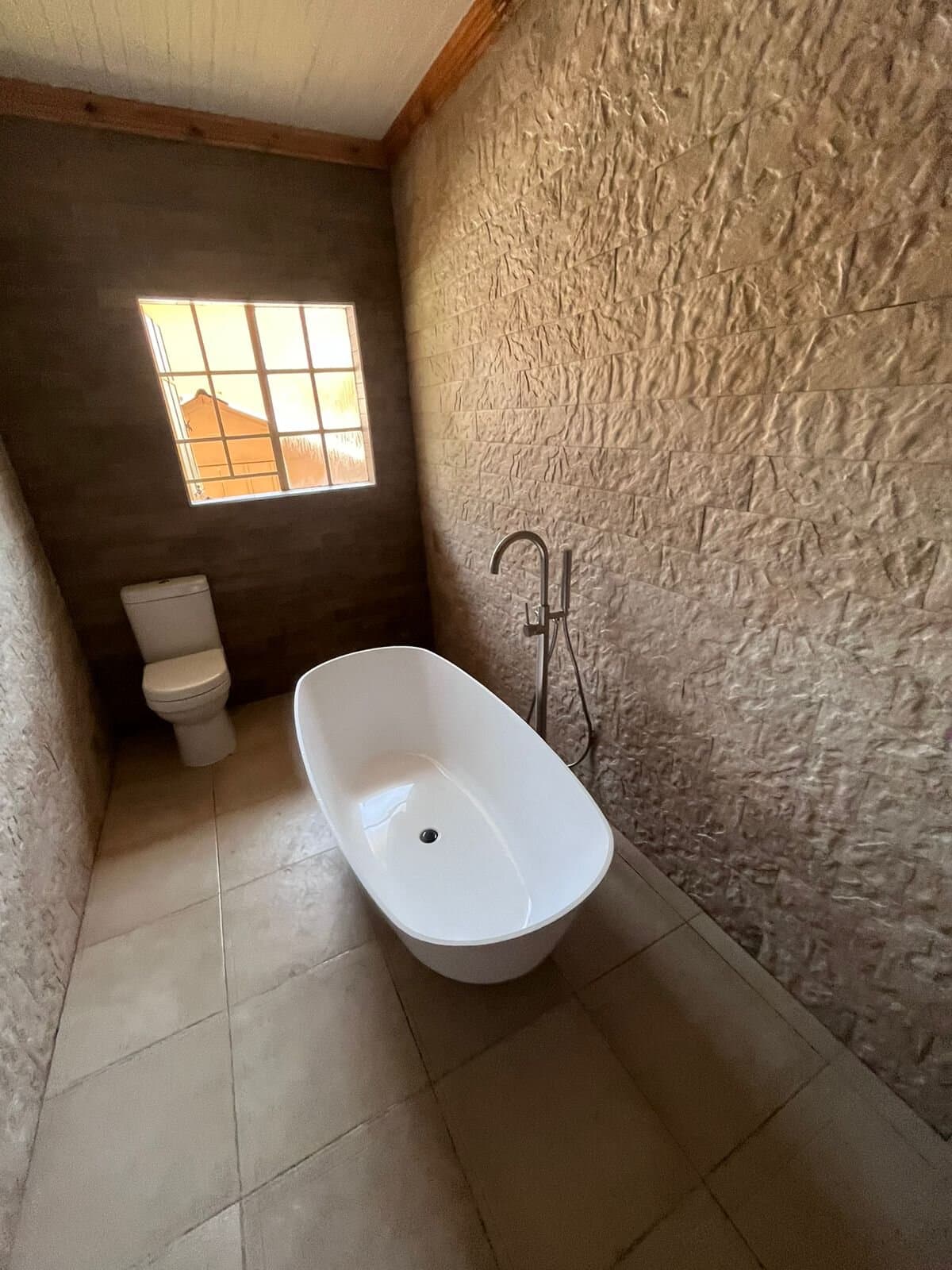 Bathroom renovation with a freestanding bath against a textured stone feature wall