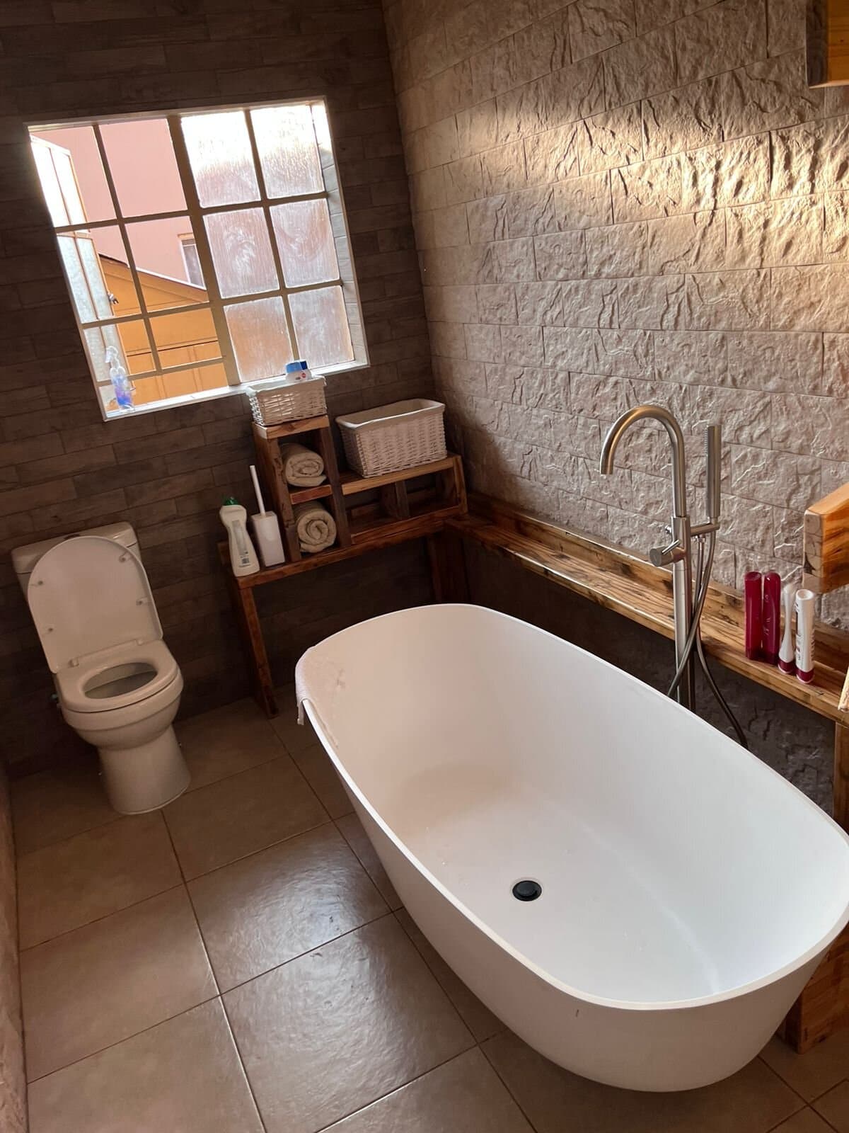 Bathroom renovation with a freestanding bath, floor-mounted mixer and timber shelving against a stone wall
