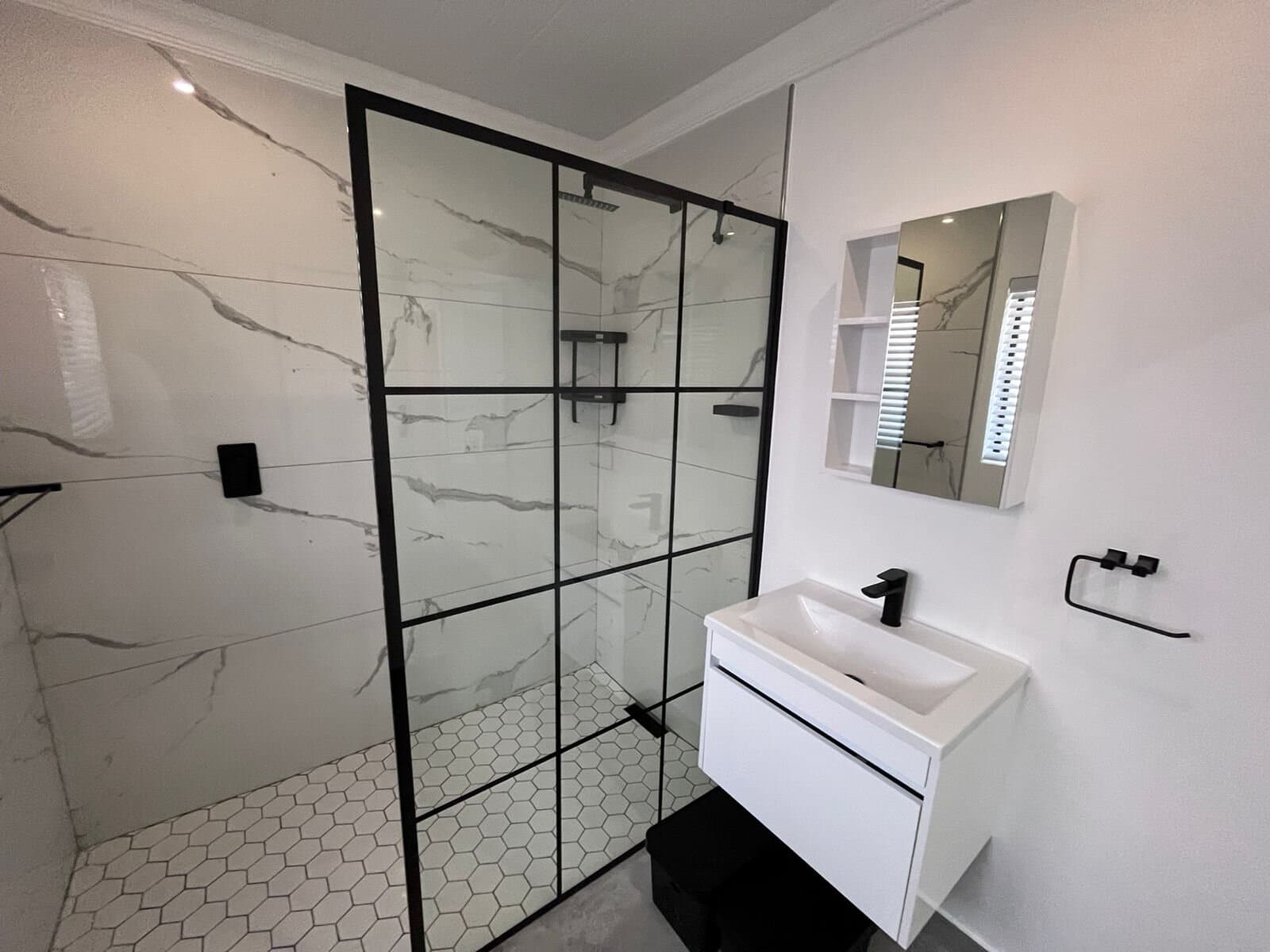 Bathroom renovation with a black-framed walk-in shower, marble-look tile and white floating vanity