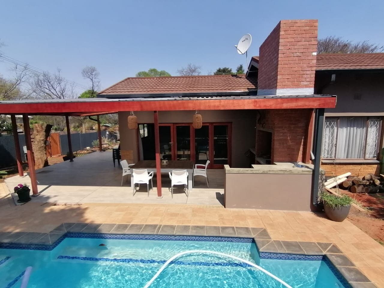 Covered outdoor patio with built-in braai and dining area next to a swimming pool